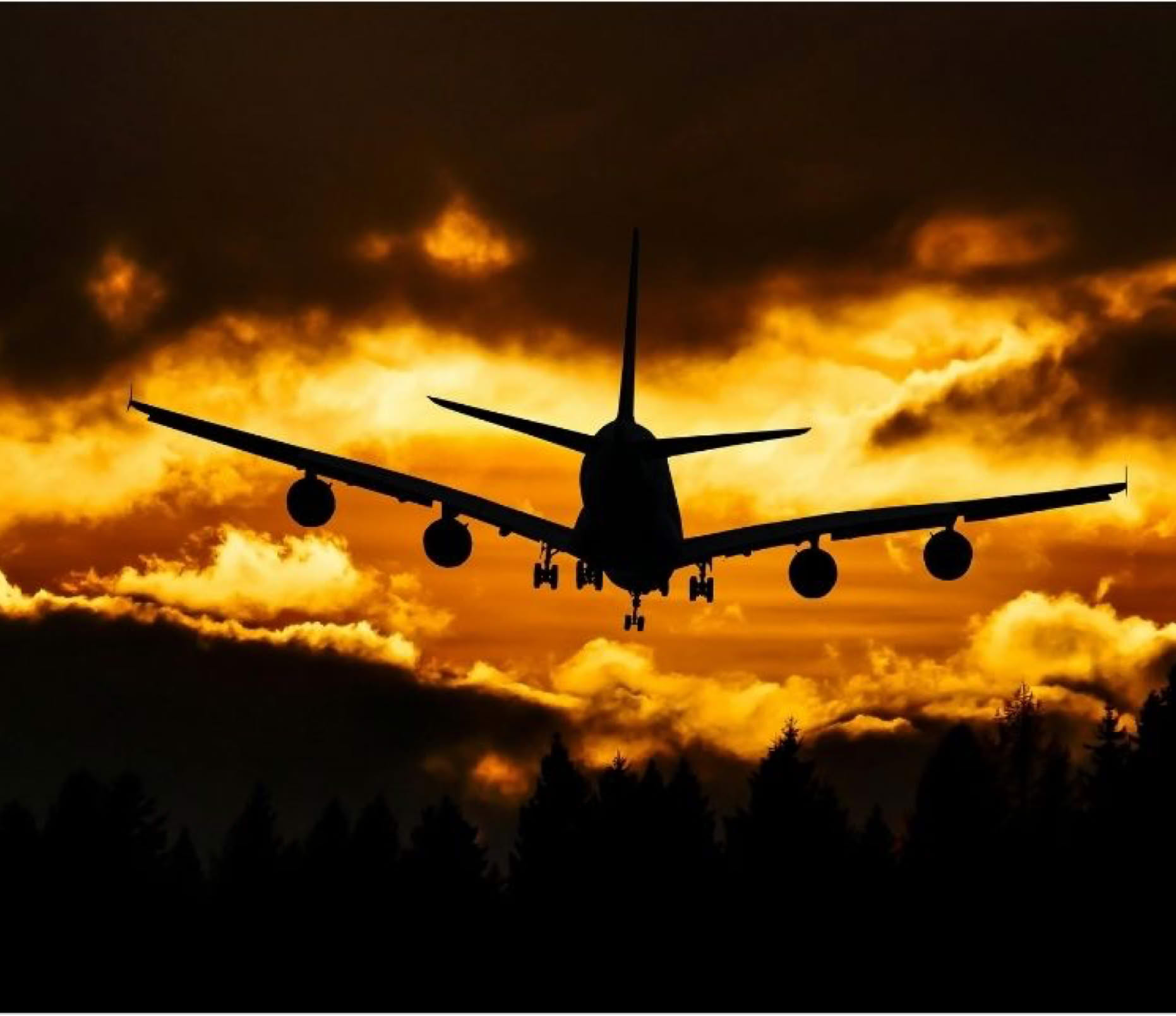 Silhouette eines Flugzeugs im Landeanflug vor einem dramatischen, orangefarbenen Himmel bei Sonnenuntergang.